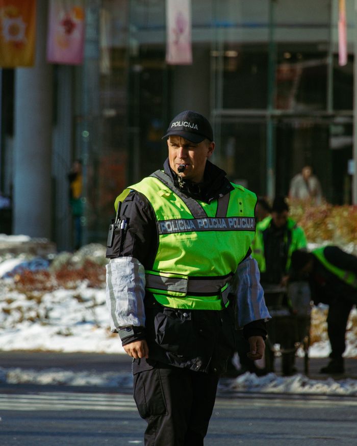 A police officer in vibrant green vest manages city traffic during a snowy winter day.