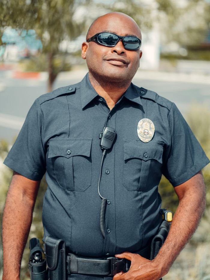 Portrait of a smiling police officer in sunglasses and uniform outdoors, exuding confidence and professionalism.