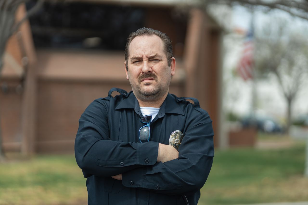 Close-up portrait of a police officer with arms crossed, standing outdoors.